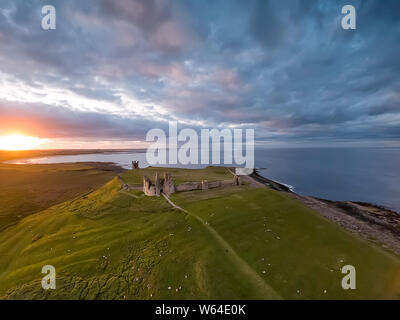 View from the air to Embleton bay, North sea, the cliff, ruins and green fields with flock of sheep. Sunset. England countryside. UK.  Aerial footage Stock Photo