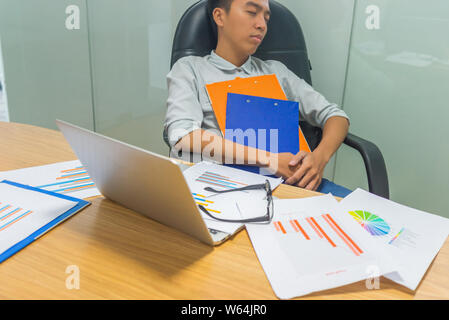 Young tired businessman falling asleep at unorganized workplace Stock Photo