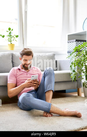 Relaxed man using phone at home sitting on the floor Stock Photo