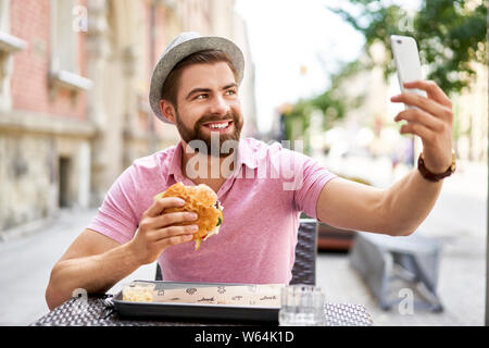 Man eating hamburger and taking selfie in the city Stock Photo