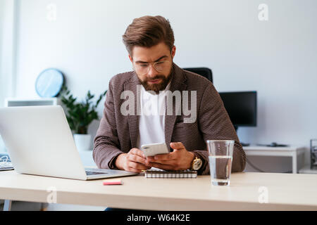Young businessman checking phone while working with laptop in home office Stock Photo