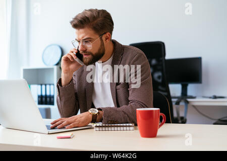 Young businessman talking on phone while working with laptop in home office Stock Photo