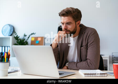 Stressed handsome man sitting in home office and looking at laptop Stock Photo