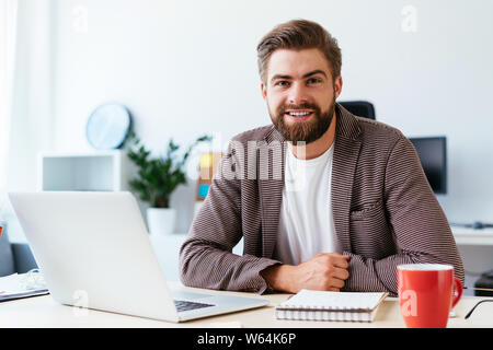 Portrait of young startup businessman sitting in small modern office and looking at camera Stock Photo