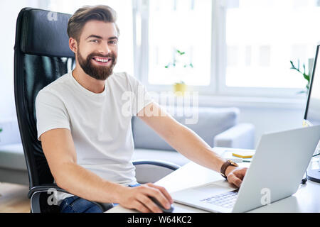 Happy student sitting by desk in his dorm room Stock Photo