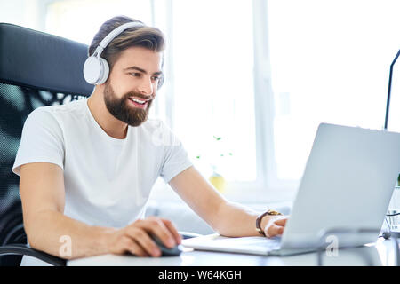 Man working on laptop with headphones from home office. Student working on laptop from dorm room Stock Photo
