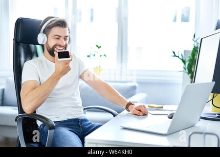 Relaxed freelancer sitting by desk talking on the phone Stock Photo