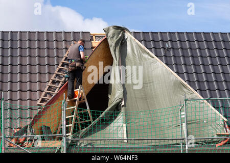 Roofer stands unsecured on a ladder Stock Photo