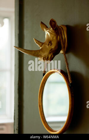 A round mirror on a brown and gold wall.Hanging on the fore head of a rhinoceros, painted in gold color. Interior design Stock Photo