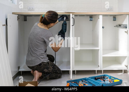 Young woman using electric screwdriver to installation kitchen furniture, DIY concept