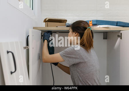 Young woman using electric screwdriver to installation kitchen furniture, DIY concept