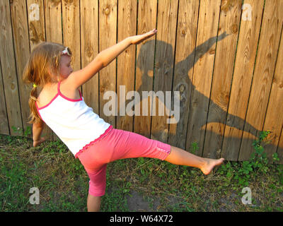 Little girl dabbling and watching shadow on fence. Child looking at her shadow on wooden fence. Little girl making figures from shadow on wooden fence Stock Photo