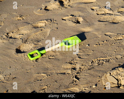 A child's plastic spade lies abandoned on the yellow sand of a Norfolk Beach adding to the plastics pollution of our seas. Stock Photo