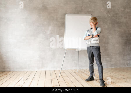 A little schoolboy in sweater and black trousers stands about with flip Board. Stock Photo