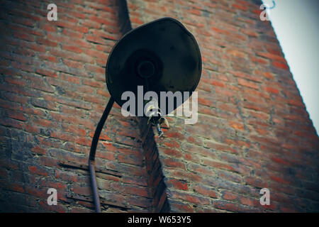 A broken rusty old lantern hangs on the wall of an abandoned brick house abandoned by people. The time of darkness and decline. Stock Photo
