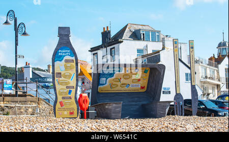 Lyme Regis, Dorset, UK. 31st July, 2019. UK Weather: A giant litter sculpture of takeaway packaging hat has been erected on the picturesque beach at the seaside resort of Lyme Regis. Consisting of an 8 foot high plastic drinks bottle, cutlery measuring 6 foot tall and a chip/burger box measuring 4x4 foot the sculptures promote the efforts of Litter Free Coast partners in promoting environmentally responsible choices. It is hoped that the temporary installation by architectural designer Jack Raisey will encourage people to take their litter home. Credit: Celia McMahon/17�Թ����� Live News Credit: Ce Stock Photo