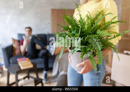 Woman in the foreground holding a fern flower in her hands. Young couple moving to a new apartment together. Relocation concept