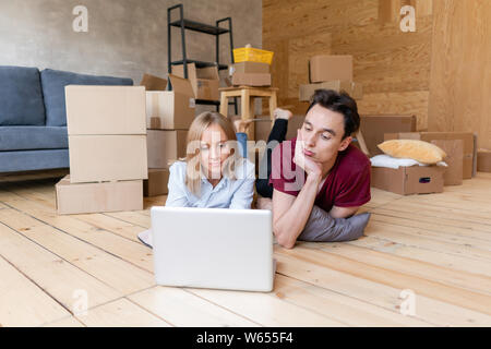 Happy Couple lying on floor together using computer wireless internet while moving into new home. Family moving to a new apartment together Stock Photo