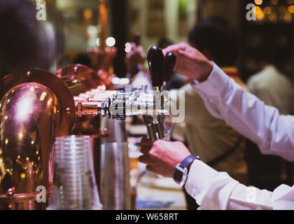 Bartender pouring draft beer in the bar, Barman hand at beer tap pouring draught lager beer serving in a restaurant or pub Stock Photo