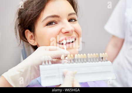 Smiling woman in the professional teeth whitening at the dentist in the selection of tooth color Stock Photo