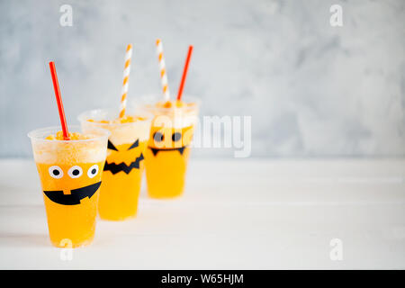 Decorated glasses with cold pumpkin orange cocktail(punch,lemonade,shake,smoothie) with cute,funny and spooky face for Halloween with copy space Stock Photo