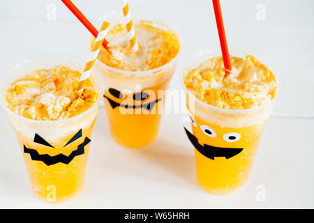 Decorated glasses with cold pumpkin orange cocktail(punch,lemonade,shake,smoothie) with cute,funny and spooky face and whipped cream for Halloween Stock Photo