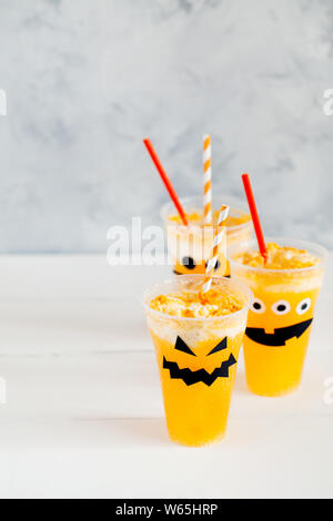 Decorated glasses with cold pumpkin orange cocktail(punch,lemonade,shake,smoothie) with cute,funny and spooky face for Halloween with copy space Stock Photo