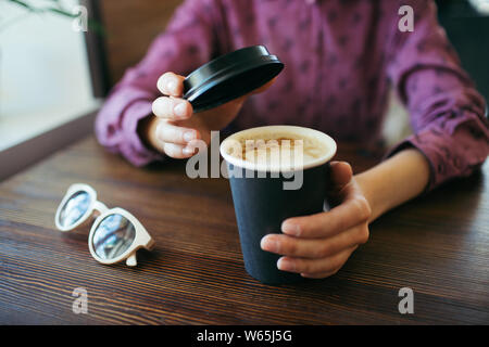 Female hands with a cup of cappuccino, with thick foam in black takeaway paper cup. Stock Photo