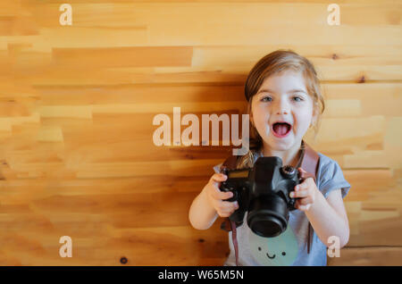 Happy excited little girl with photocamera on light wooden background. Stock Photo