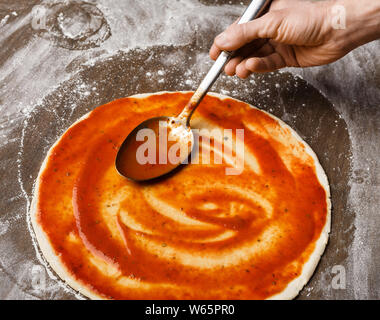 Spreading tomato sause on pizza base, closeup Stock Photo