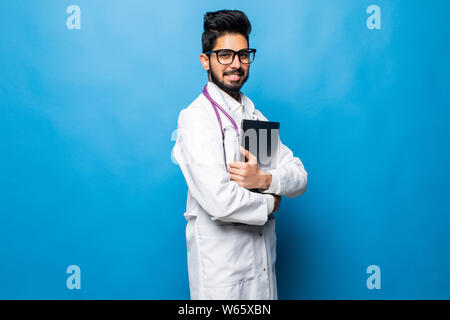Indian doctor standing in the studio while working with laptop, isolated on blue background Stock Photo