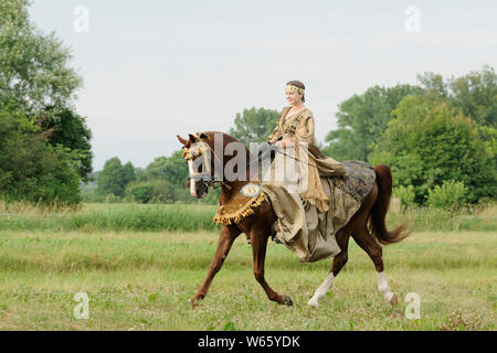 Horsewoman in historic dress on troted chestnut Arabian horse stallion Stock Photo