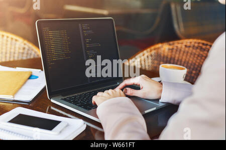 Young woman programmer writing code on laptop in cafe Stock Photo