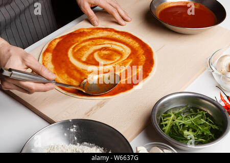 Chef spreading tomato paste on pizza base Stock Photo