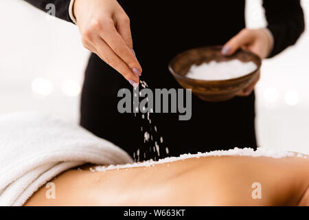 Beauty therapist pouring salt scrub on woman back at health spa Stock Photo