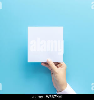 woman hand holding blank paper sheet isolated on blue background with copy space. Stock Photo