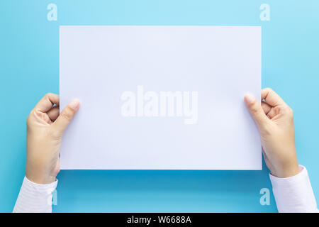 close up hands holding  empty white blank letter paper size A4 for flyer or invitation mock up isolated on a blue background. Stock Photo