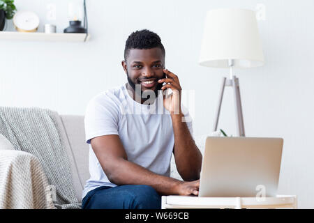 Black man working on laptop and calling Stock Photo