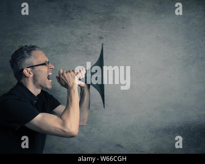 Young man holding a big horn, speaking loud concept on a dark studio background with space for text or image Stock Photo