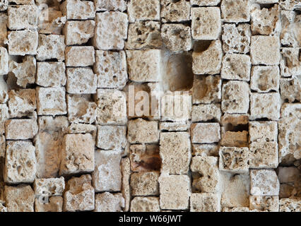 Seamless pattern of partially destroyed masonry wall of limestone blocks. Background texture of weathered ancient brick wall. Gaps from broken stones Stock Photo