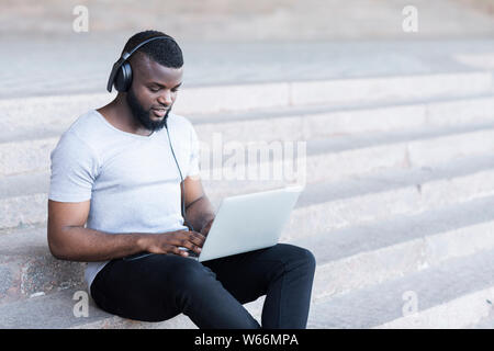 Young bearded african guy in headphones coding on laptop Stock Photo