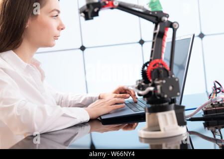 A young woman writes an algorithm for the robot arm. Science Research Laboratory for Robotic Arm Model. Computer Laboratory Stock Photo