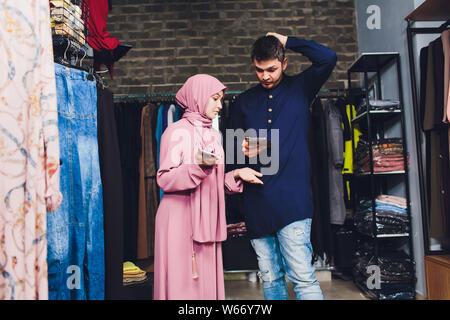 Portrait of a muslim businesswoman checks availability of goods by using the touch pad while standing in her modern shop, young female consultant Stock Photo