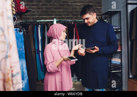 Portrait of a muslim businesswoman checks availability of goods by using the touch pad while standing in her modern shop, young female consultant Stock Photo