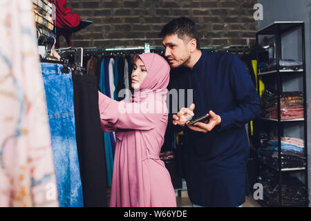Portrait of a muslim businesswoman checks availability of goods by using the touch pad while standing in her modern shop, young female consultant Stock Photo