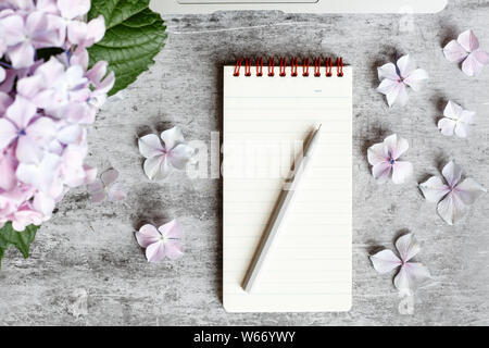 Home office desk workspace with laptop, hydrangea flowers bouquet, accessories on gray marble background. Flat lay, top view decorated mockup. Stock Photo