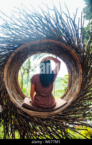A female tourist is sitting on a large bird nest on a tree at Bali island, Indonesia Stock Photo