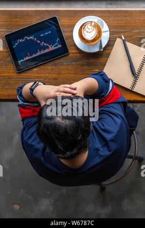 Young Asian investor having headache while watching stock trading graph Stock Photo