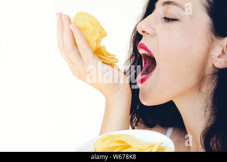 Hungry attractive girl eats a lot of French fries, holds a handful of snacks and puts it in the mouth. Close-up portrait of a girl greedily eats Frenc Stock Photo