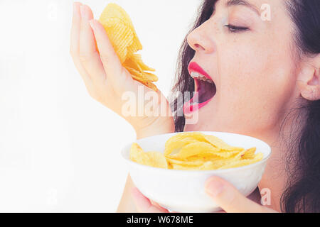 Hungry attractive girl eats a lot of French fries, holds a handful of snacks and puts it in the mouth. Close-up portrait of a girl greedily eats Frenc Stock Photo